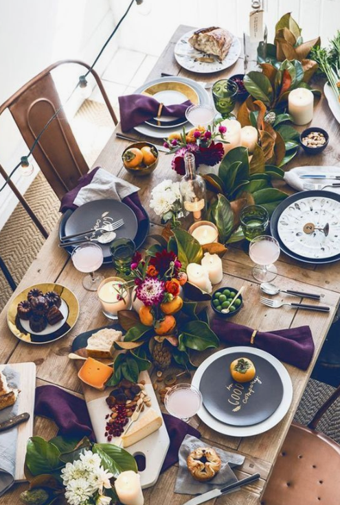 a bright and natural fall tablescape with fall fruits, blooms, foliage, pillar candles and printed dark plates