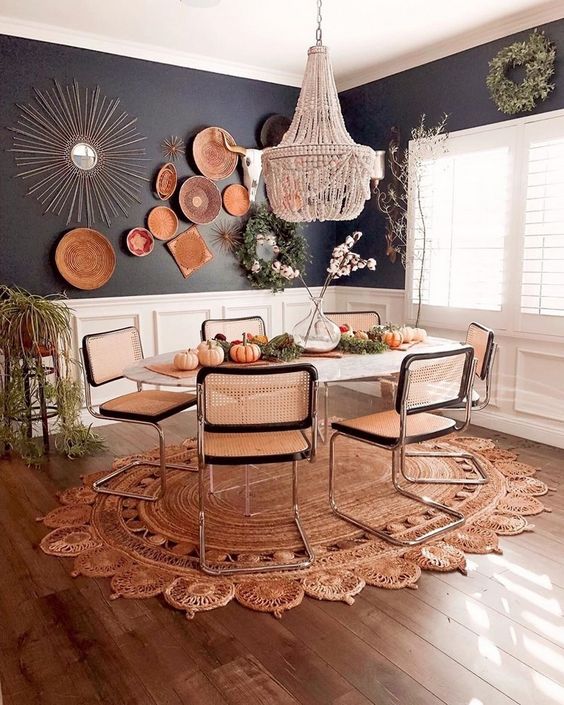 a bright boho dining room with a beaded chandelier, wicker chairs, a jute rug, decorative plates and greenery
