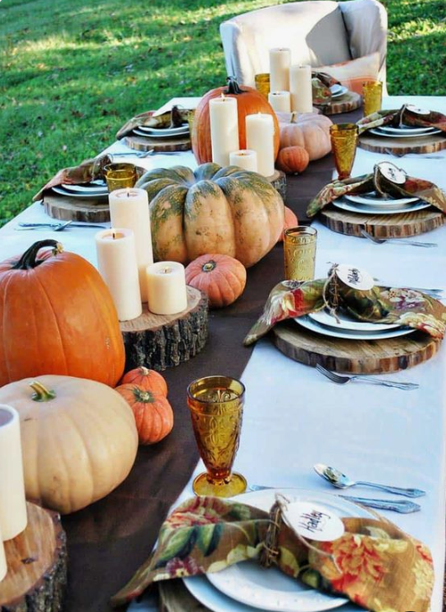 a bright fall table with a brown runner, wood slice placemats, natural pumpkins and pillar candles