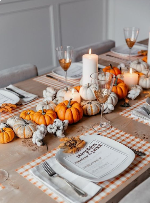 a colorful fall table with plaid placemats, bright pumpkins and cotton, pillar candles and fall leaves instead of place cards