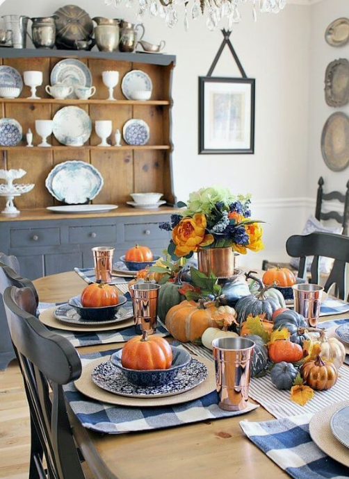 a colorful fall tablescape with a striped runner and plaid placemats, colorful pumpkins and copper mugs and vases