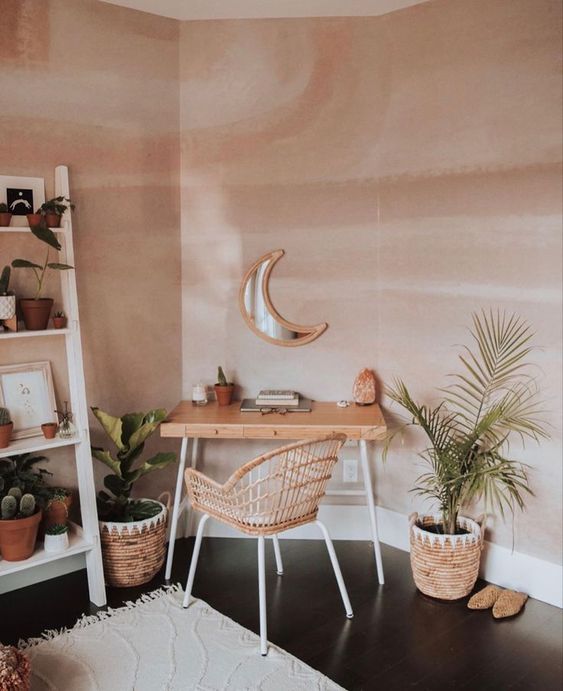 a cozy boho home office nook with a small desk and a rattan chair, potted plants, a ladder with plants and cacti, a neutral rug