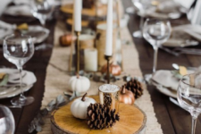 a cozy fall table setting with a fabric runner, wood slices, pinecones, candles and mini pumpkins