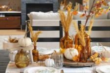 a cozy fall tablescape with a plaid tablecloth, amber glasses and bottles, white pumpkins and fall leaf and herb arrangements