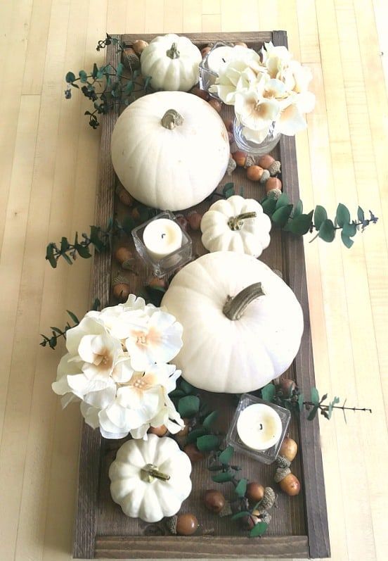 a dark stained woodne tray, white pumpkins, blooms, candles and acorns for a pretty fall centerpiece