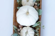 a dough bowl with pumpkins, eucalyptus and acorns is a cool fall centerpiece with a strong rustic feel
