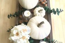 a fall centerpiece of a dark tray with white candles, white blooms and pumpkins, acorns and eucalyptus