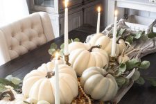 a fall centerpiece of a table runner, pumpkins, gourds, antlers, candles and beads is veyr lush and chic