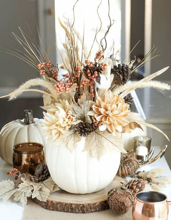 a fall centerpiece of a white pumpkin as a vase, dried leaves, blooms, twigs, berries and wheat