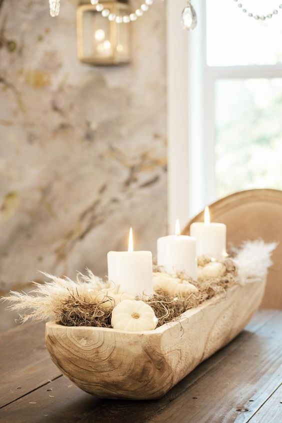 a fall centerpiece of a wooden box with hay, pampas grass, pumpkins and pillar candles is very stylish