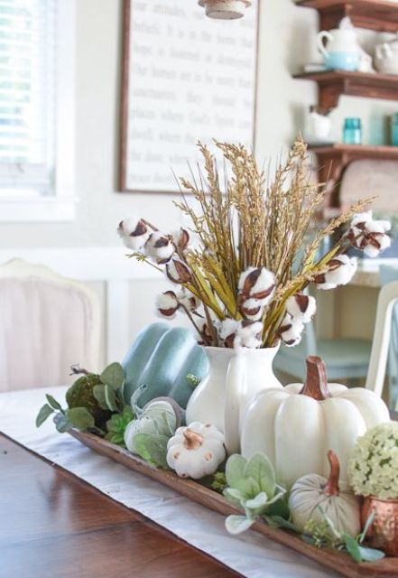 a fall centerpiece with fake pumpkins, greenery, succulents, herbs and cotton in a simple white jug