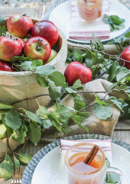 a fall tablescape with foliage, apples, burlap and blue chargrers plus fall drinks