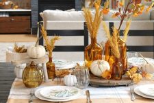 a fall tablescape with pumpkins, leaves, wheat on stands and trays looks very inviting and very cozy