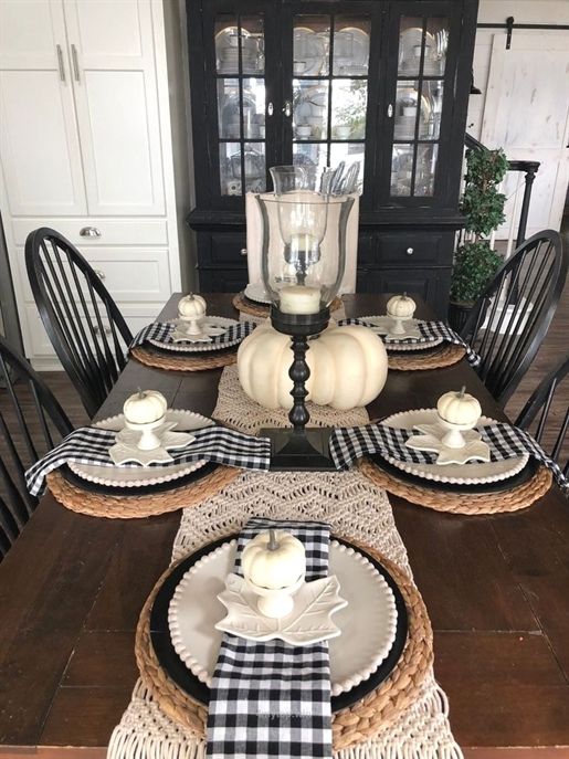 a farmhouse fall table setting with a macrame runner, woven placemats, plaid napkins and fake pumpkins