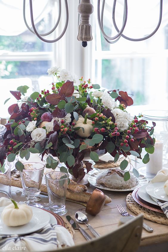 a gorgeous fall centerpiece of eucalyptus, dark foliage, berries, white blooms and pumpkins and fruit