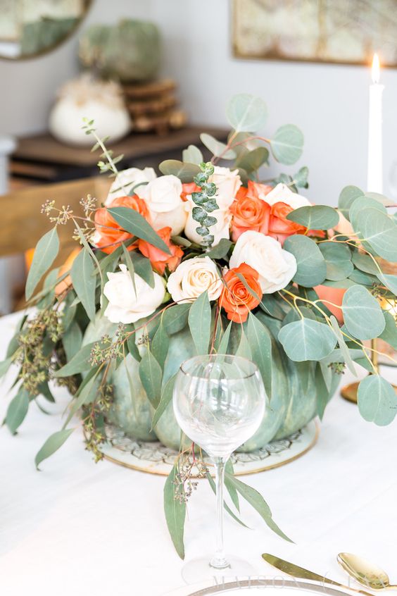a green pumpkin with blush and orange roses and various types of eucalyptus is a natural and chic centerpiece for the fall