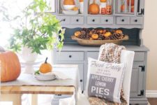 a grey buffet with lots of orange pumpkins, a dough bowl with pinecones and faux orange pumpkins