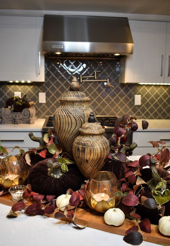 A jewel toned fall decoration with burgundy leaves, candles, white pumpkins and wooden jars