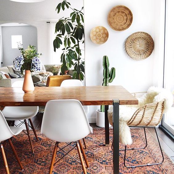 a light-filled boho dining space with decorative plates, greenery,a boho rug, white chairs and a sleek table