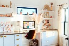 a light-filled boho home office with a desk with plenty of storage, open shelves, a boho rug, a macrame chandelier and pampas grass