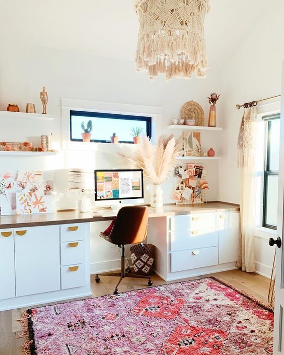 A light filled boho home office with a desk with plenty of storage, open shelves, a boho rug, a macrame chandelier and pampas grass