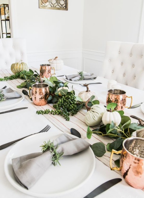 a lively fall tablescape with a striped runner, greenery and neutral pumpkin plus copper mugs