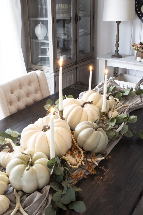 a lovely fall centerpiece of a wooden tray, white pumpkins, greenery, candles and wooden beads is very beautiful