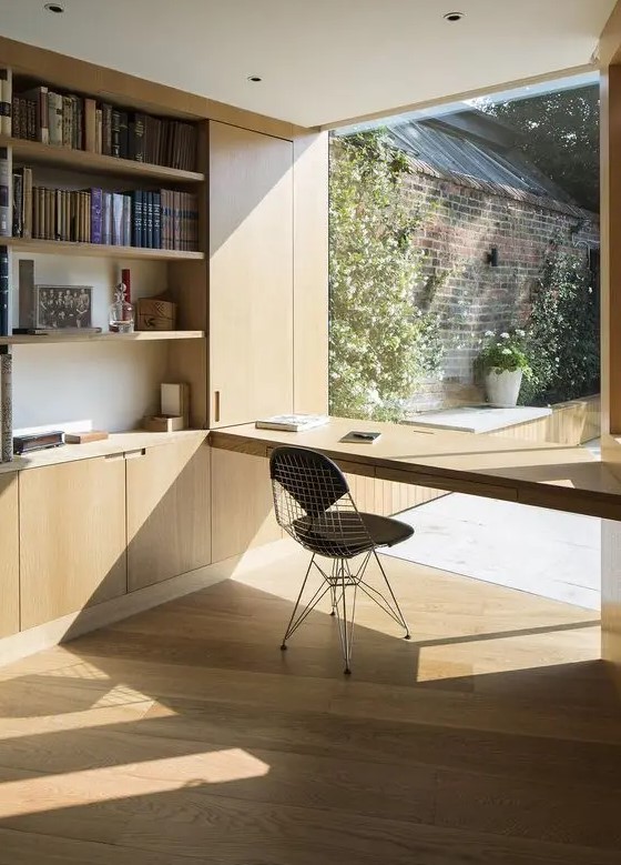 A minimalist home office with a built in plywood storage unit with open storage compartments, a windowsill desk and a black chair