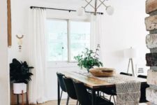 a modern boho dining room with black chairs, a sleek wooden table, a macrame table runner and greenery