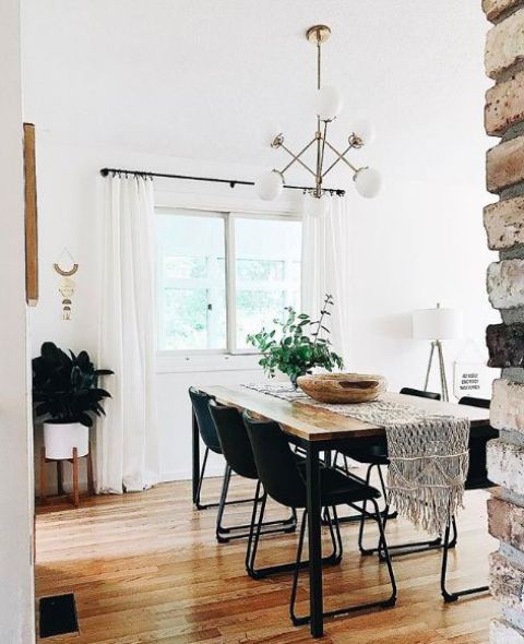 a modern boho dining room with black chairs, a sleek wooden table, a macrame table runner and greenery