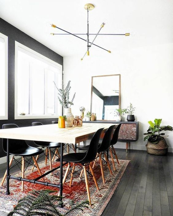 a modern boho dining space with a sleek wooden table, black chairs, a boho rug, an inlay sideboard and a catchy chandelier