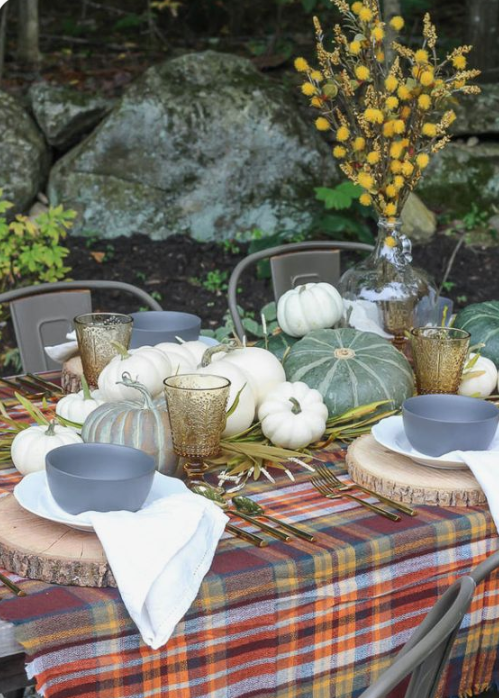 a natural fall table with a plaid tablecloth, wood slice placemats, natural pumpkins, herbs and a billy ball centerpiece