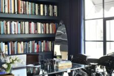 a navy home office with a coffered ceiling, built-in storage space, a glass and metal desk plus a bike as decor