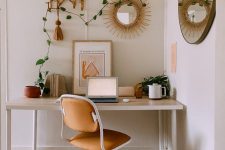 a neutral boho chic home office with a boho rug, a desk, a leather chair, hats, a rattan shelf and a sunburst mirror