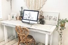 a neutral boho home office with a whitewashed desk, a unique rattan chair, a macrame hanging, potted plants and artworks