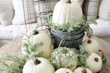 a neutral fall centerpiece of a basket with greenery, white pumpkins and a bucket with a pumpkin