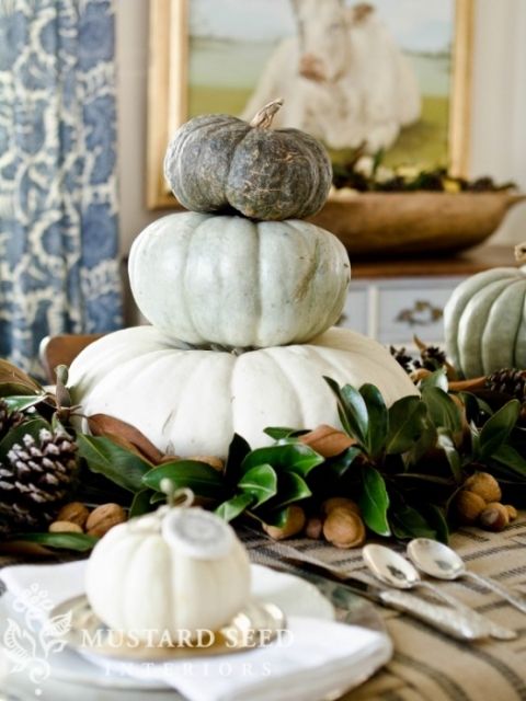 a neutral fall centerpiece of magnolia leaves, nuts, pinecones and a stack of pumpkins is cool