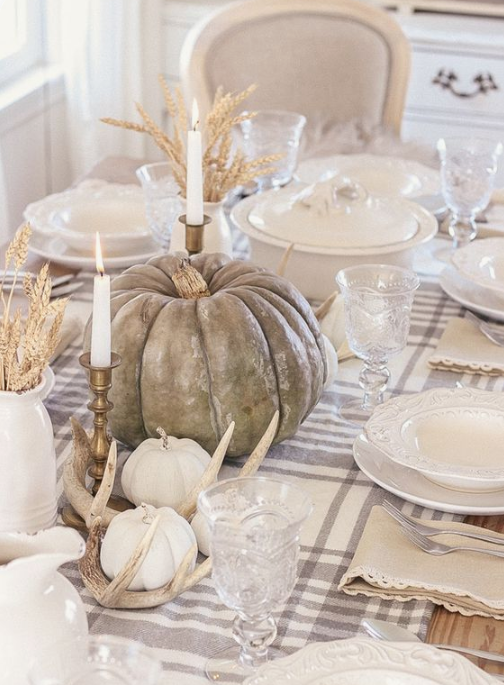 a neutral fall table with natural pumpkins, antlers, tall candles, wheat in jugs, white porcelain and a plaid table runner