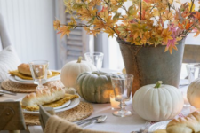 a neutral fall table with woven placemats, a fall leaf centerpiece, natural pumpkins and candles for coziness