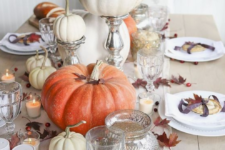 a neutral fall tablescape with a white table runner, cranberries, leaves, fresh pumpkins and candles
