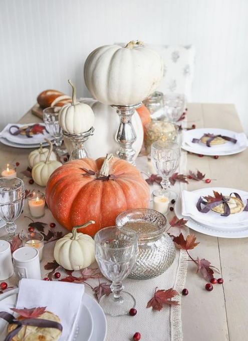 a neutral fall tablescape with a white table runner, cranberries, leaves, fresh pumpkins and candles