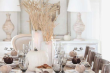 a neutral farmhouse tablescape with a lace runner, wheat arrangements, neutral pumpkins and velvet ones to mark eahc place setting