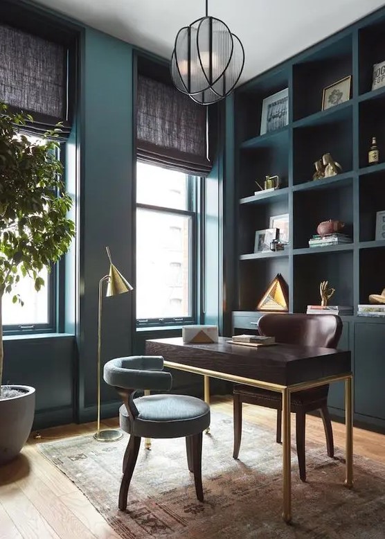a refined teal home office with a built-in storage unit, a dark-stained desk and a brown chair, a grey chair and gilded touches