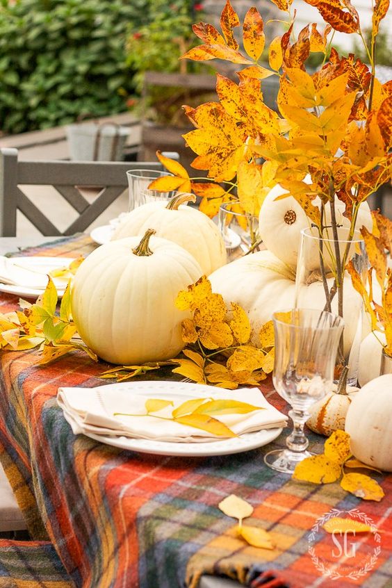 a relaxed and bright fall centerpiece of white pumpkins and bright yellow fall leaves in vases is very cool