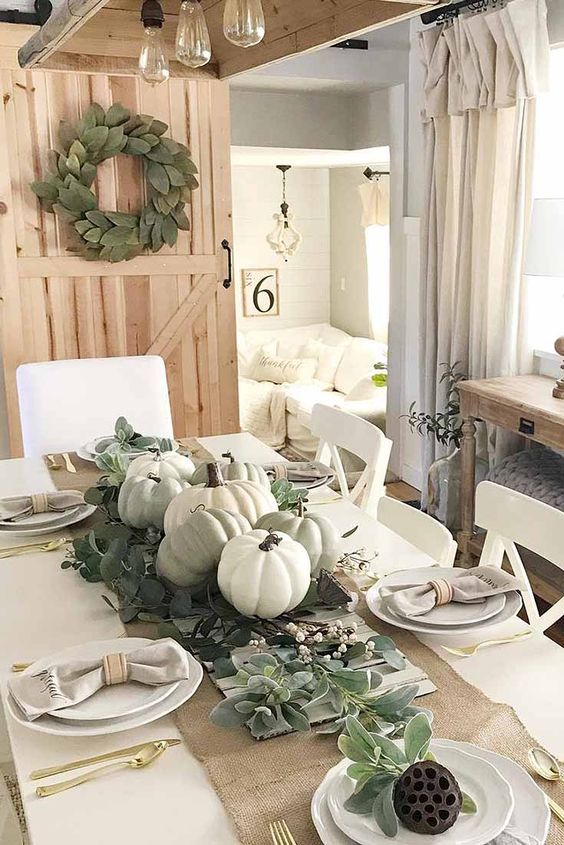 a relaxed neutral fall centerpiece of pale greenery, neutral pumpkins and wax flowers is a cool idea for your tablescape