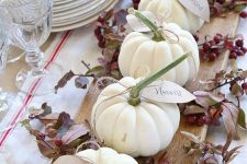 a rustic centerpiece of a wooden board, branches with berries, white pumpkins with tags is lovely for the fall