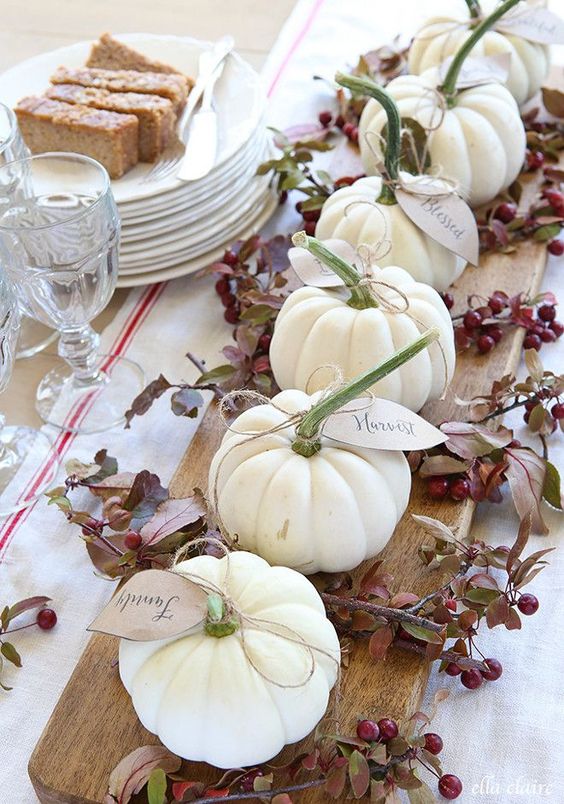 a rustic centerpiece of a wooden board, branches with berries, white pumpkins with tags is lovely for the fall