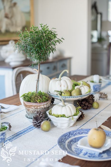 a rustic fall centerpiece of white pumpkins, pears, moss, a potted tree and pinecones all around for a cool look