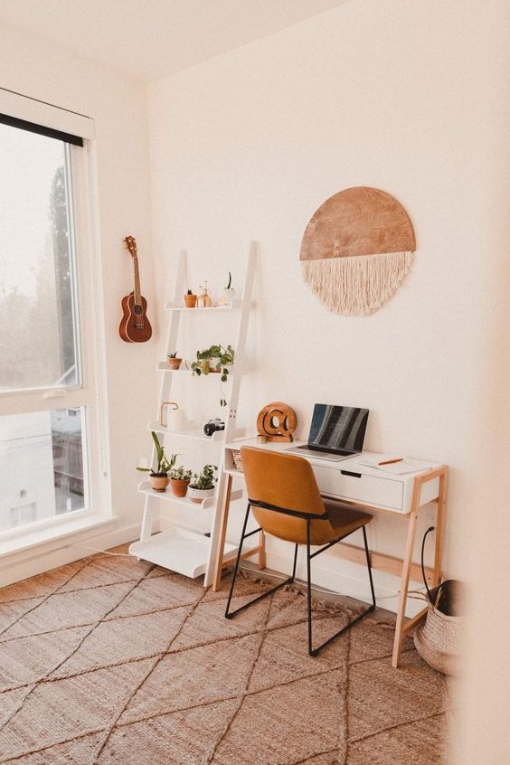 a simple and cozy boho home office with an open storage unit, a desk, a leather chair, a macrame hanging and potted plants