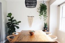 a simple boho dining room with a macrame hanging, a black wicker pendant lamp, wooden furniture and potted greenery and cacti